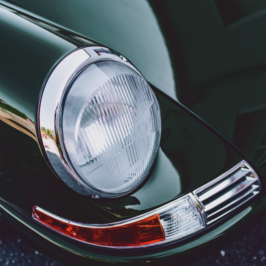 Close-up van de strakke groene voorkant van een vintage auto, met een smetteloze chromen bumper en een grote, ronde koplamp.